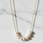 Pearl necklace on a gold chain against a marble background