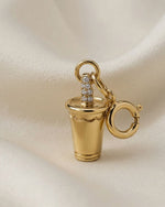 Gold charm resembling a cocktail glass with a diamond-studded band on a beige fabric background