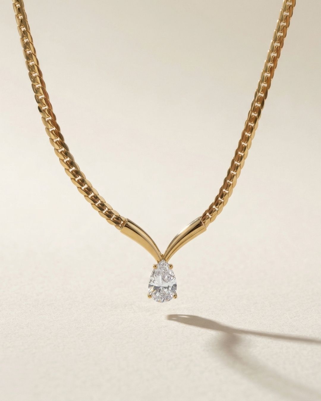 Gold necklace with a teardrop-shaped diamond pendant on a beige background
