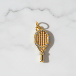 Gold tennis racket charm with rhinestones on a marble background