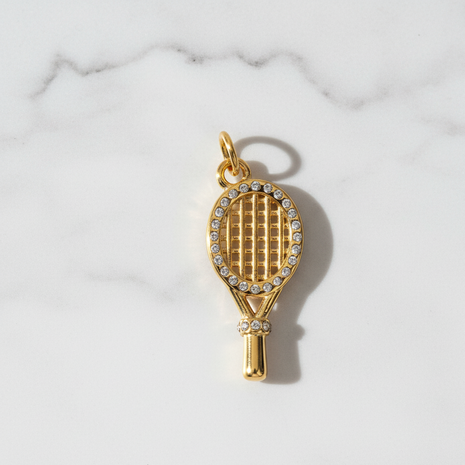 Gold tennis racket charm with rhinestones on a marble background