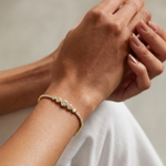Gold bracelet with diamonds on a wrist against a neutral background