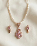 Pearl necklace with pink gemstone pendant and matching earrings on a light background
