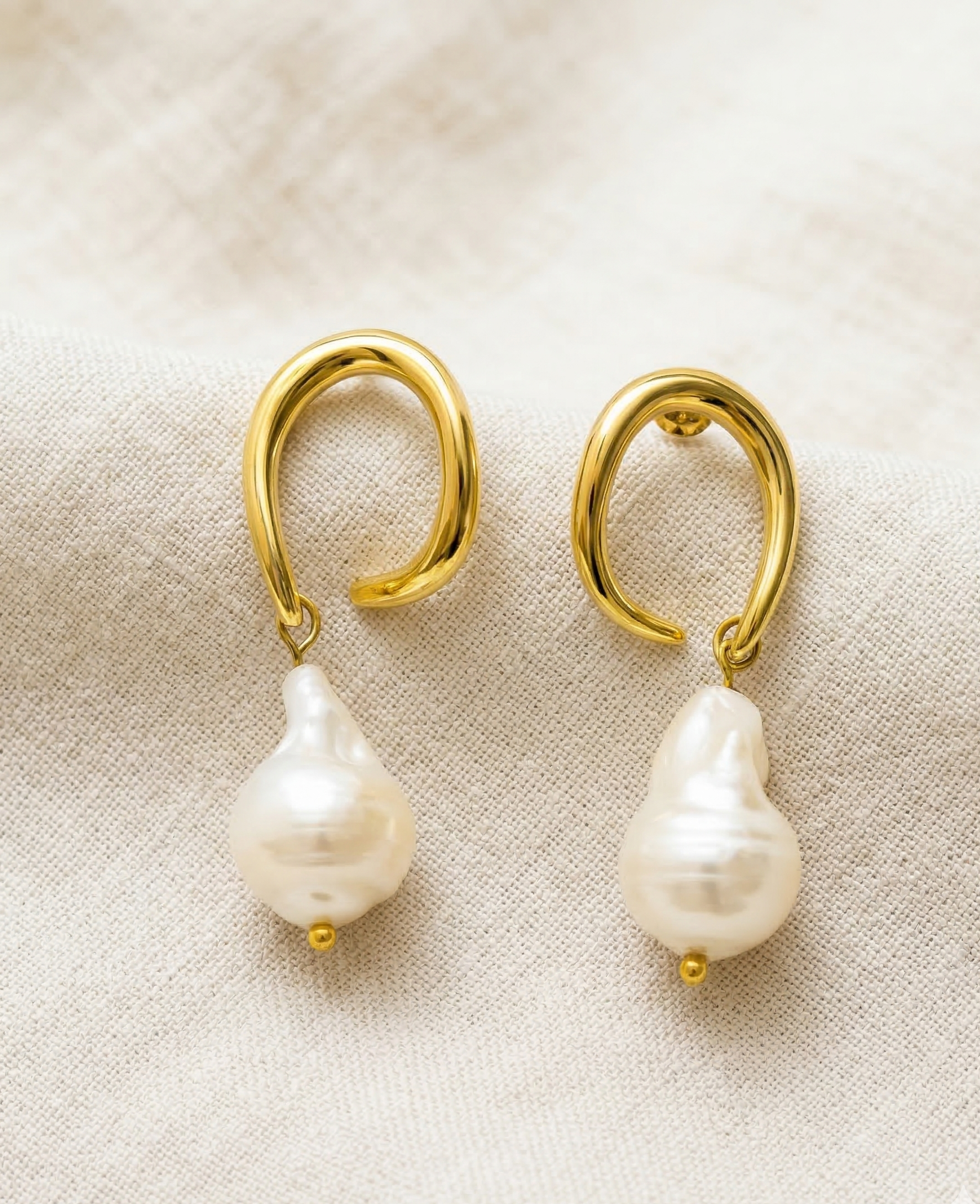 Pair of pearl earrings with gold hooks on a beige fabric background