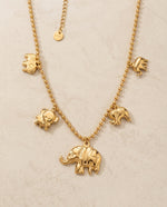 Gold necklace with elephant pendants on a beige background