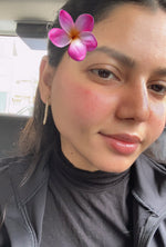 Person with a pink flower in their hair, wearing a gray jacket and black turtleneck.