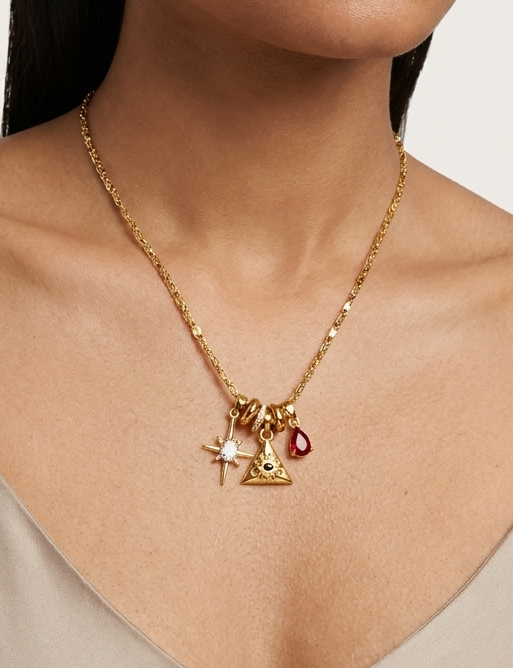 Woman wearing a gold necklace with charms on a plain background