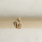 Gold ring with three diamond-studded bands on a beige cushion against a light gray background