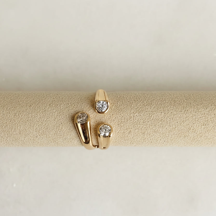 Gold ring with three diamond-studded bands on a beige cushion against a light gray background