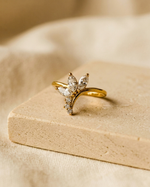 Gold tiara-shaped ring with diamonds on a beige stone surface