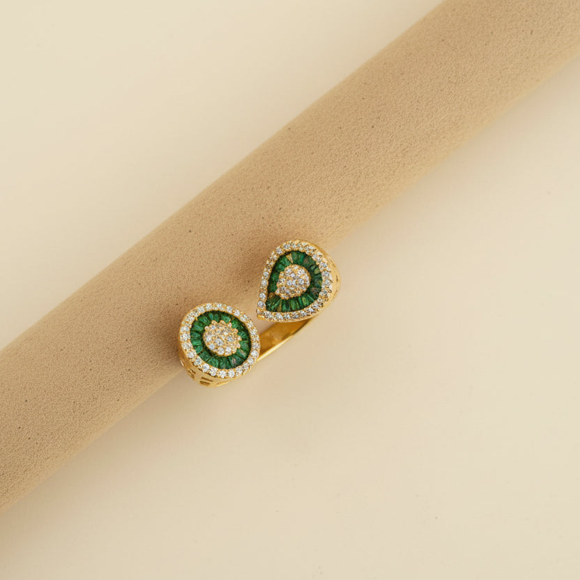 Gold earrings with green gemstones on a beige cylindrical object against a light background