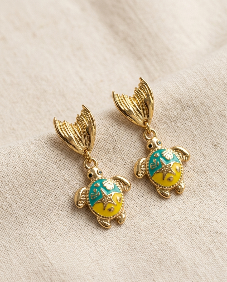 Turtle-shaped earrings with gold accents on a beige fabric background