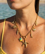 Woman wearing a gold necklace with various charms by the water