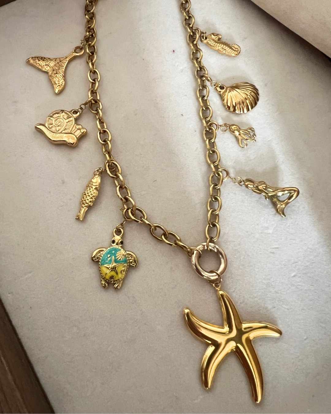 Gold charm necklace with turtle and starfish pendants on a light background