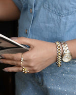 Close-up of a person's hand wearing two gold watches and a ring, holding a book.