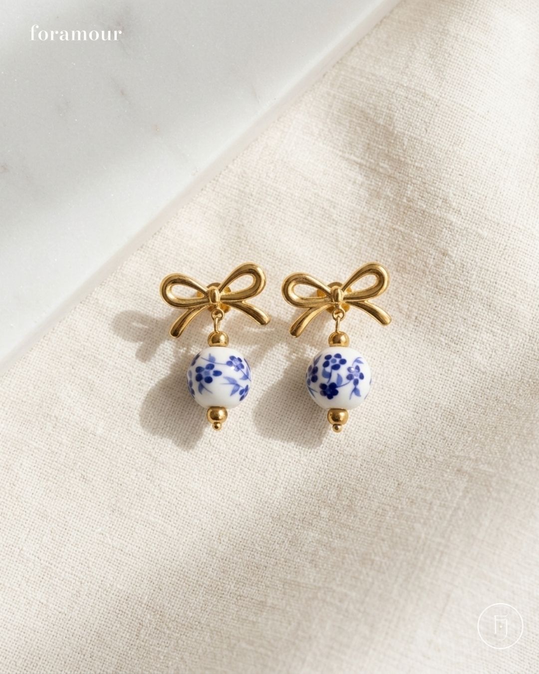 Pair of earrings with gold bows and blue floral beads on a beige fabric background