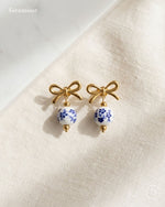 Pair of earrings with gold bows and blue floral beads on a beige fabric background