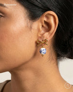 Gold bow-shaped earring with a blue and white bead worn by a person.