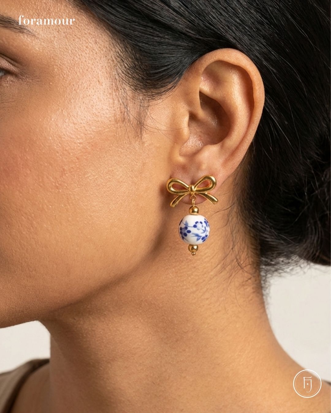 Gold bow-shaped earring with a blue and white bead worn by a person.