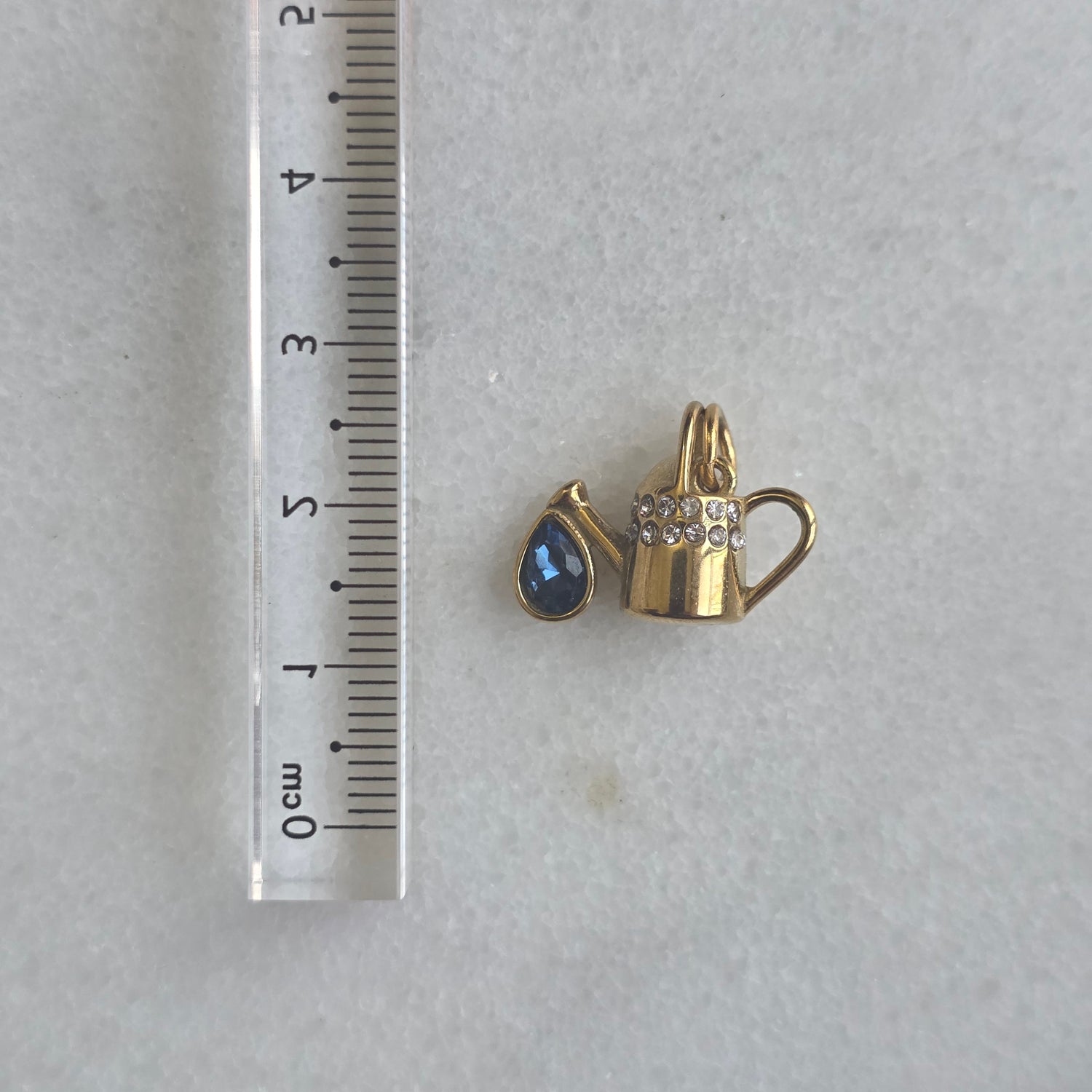 Gold charm with green gemstone and diamond-studded band on a white marble background