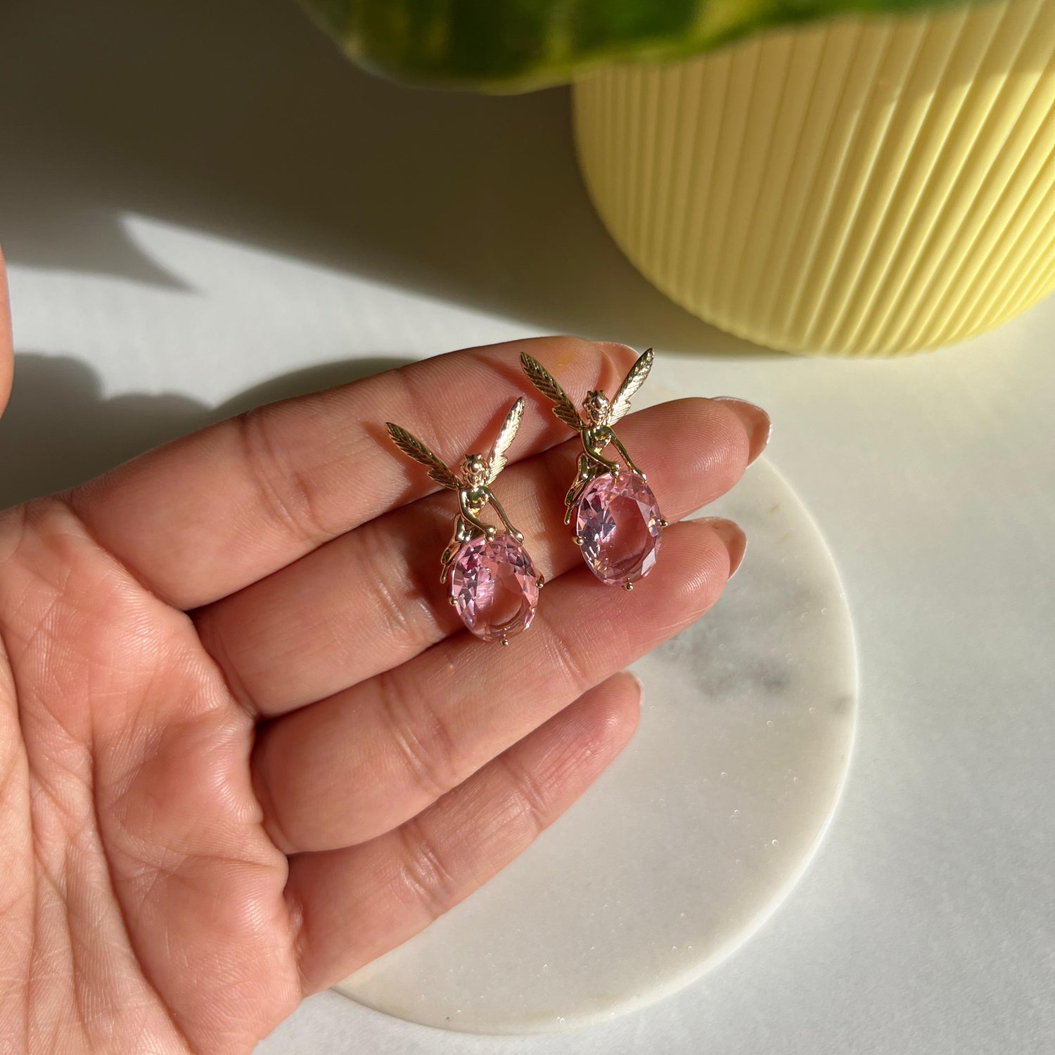 Pink earrings held in a hand with a light background