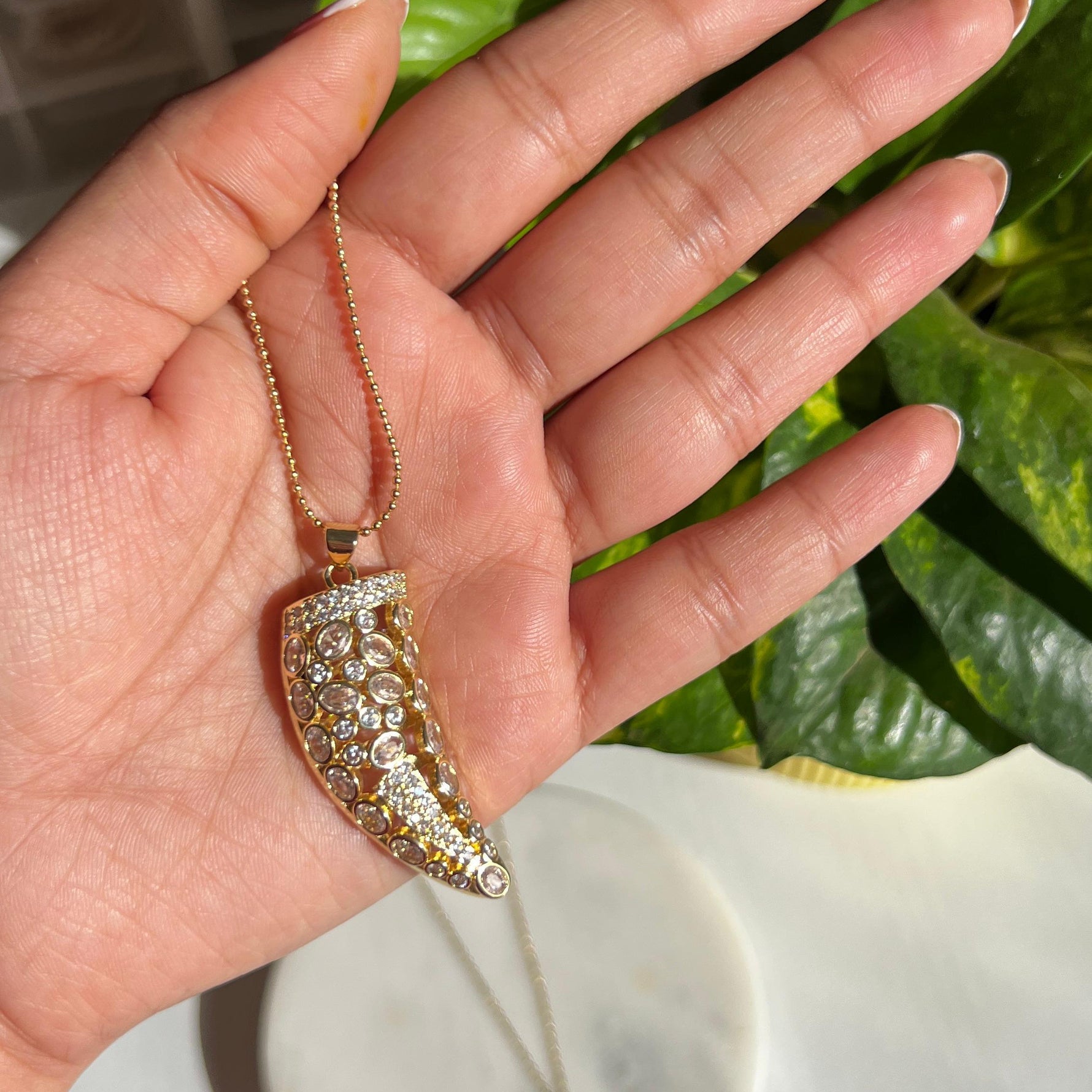 Hand holding a necklace with a decorative pendant against a blurred background