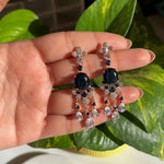 Earrings with blue gemstones held between fingers against a green leafy background