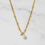 Gold necklace with a pearl pendant on a light gray background