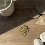 Gold leaf charm on a wooden surface with leaves and stones