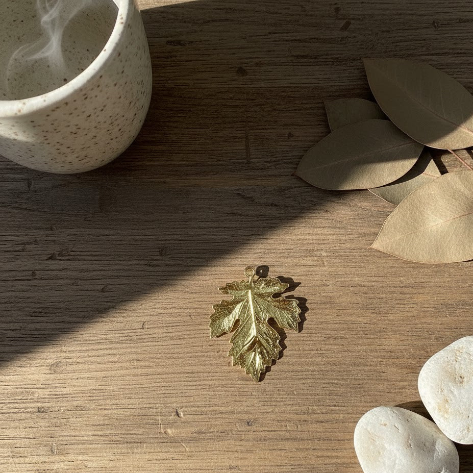 Gold leaf charm on a wooden surface with leaves and stones