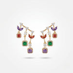 Long gold drop earrings with purple, red, emerald and amethyst halo stones stacked vertically on white surface