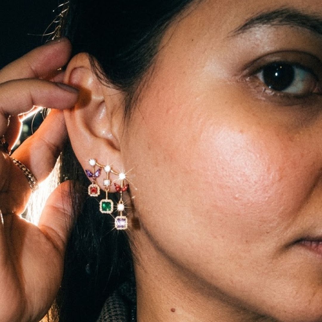 Long gold drop earrings with purple, red, emerald and amethyst halo stones stacked vertically on a model