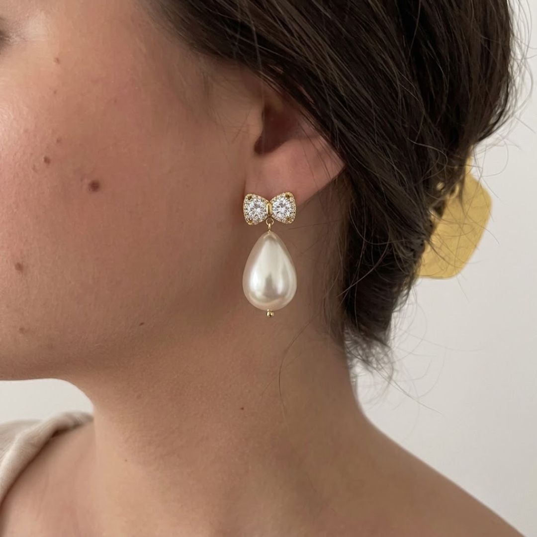 Gold CZ bow stud earrings with large teardrop baroque pearl drop on a model