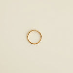Rose Gold ring on a light gray surface with a beige textured object partially visible.