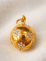 Gold football locket with diamond embellishments on a beige fabric background
