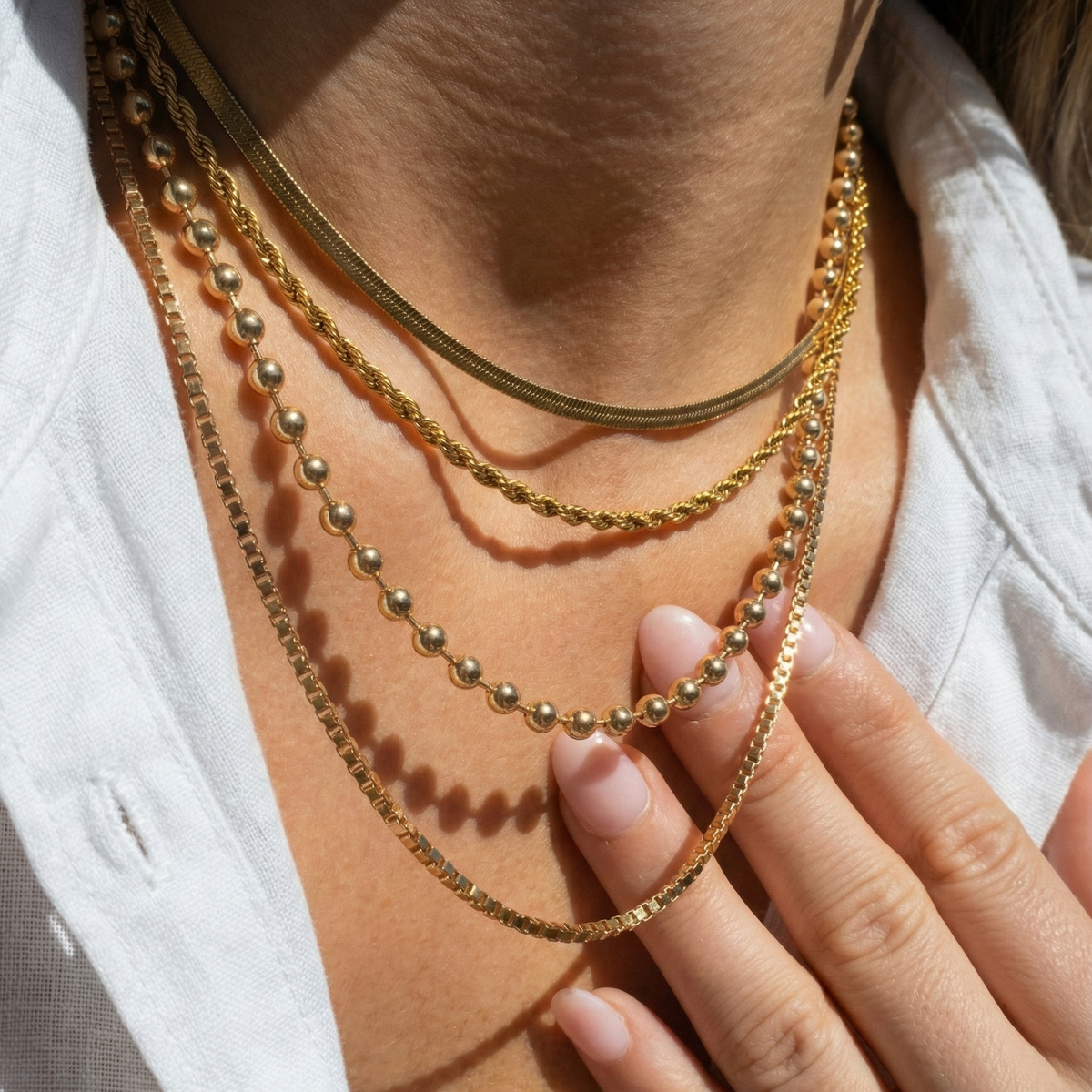 Close-up of a person wearing multiple gold necklaces with a hand resting on the chest.