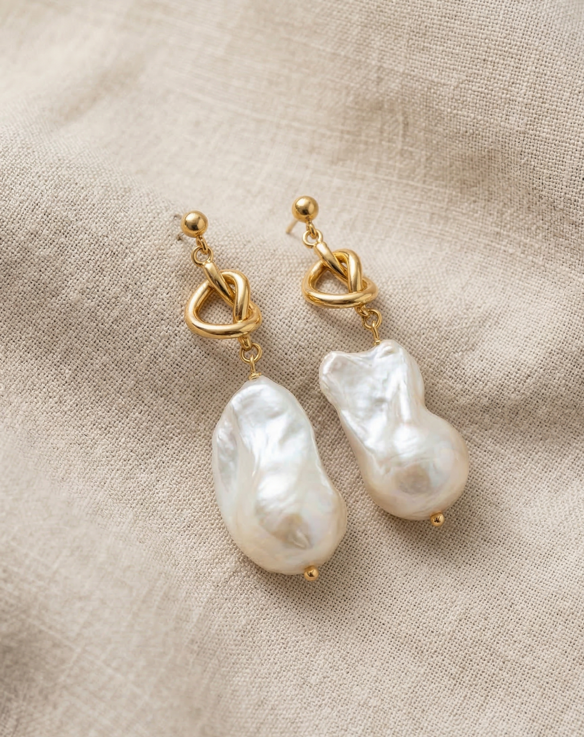 Pearl earrings with gold hooks on a beige fabric background