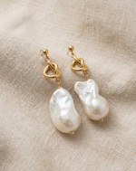 Pearl earrings with gold hooks on a beige fabric background