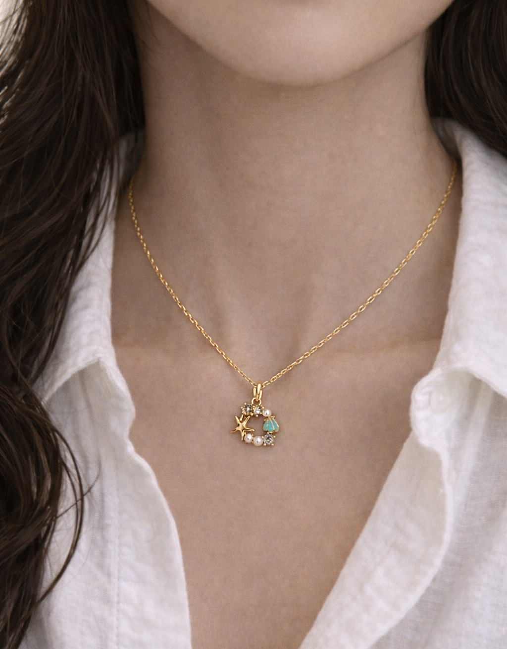 Gold necklace with a pendant worn by a person against a white shirt background