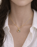 Gold necklace with a pendant worn by a person against a white shirt background
