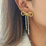 Gold bow-shaped earring with pearl details worn by a person.