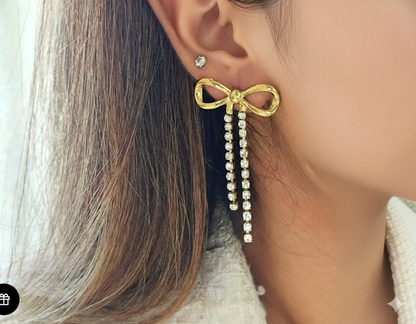 Gold bow-shaped earring with pearl details worn by a person.
