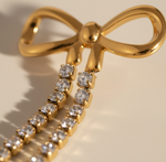 Gold bow-shaped earring with diamond accents on a beige background