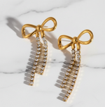 Gold bow-shaped earrings with diamond accents on a marble surface