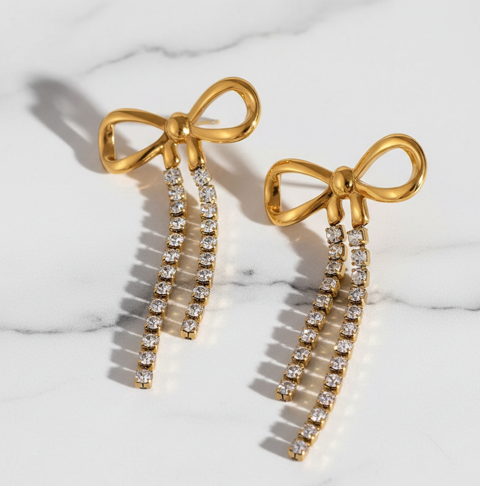 Gold bow-shaped earrings with diamond accents on a marble surface