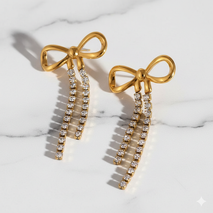 Gold bow-shaped earrings with diamond accents on a marble surface