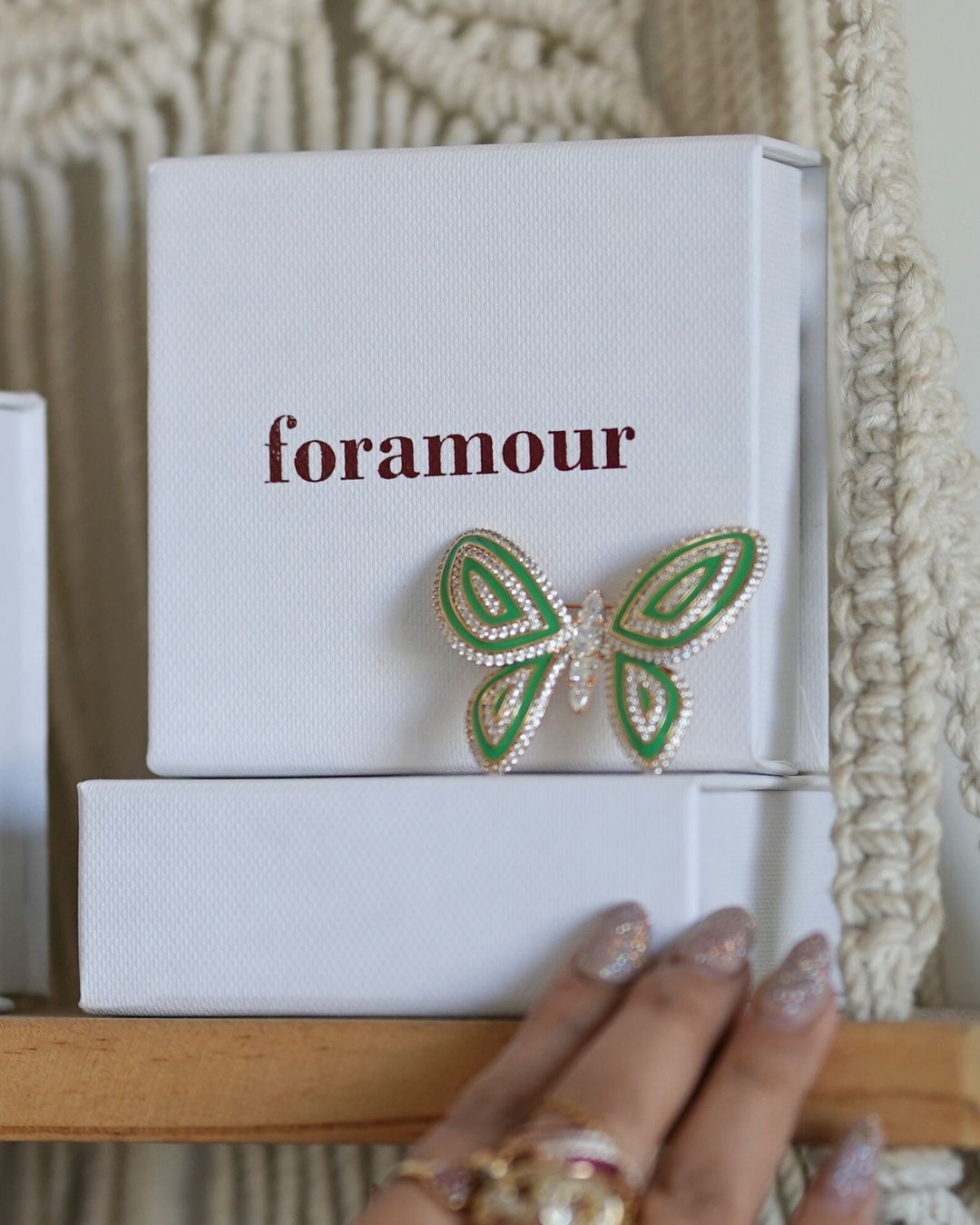 Green butterfly brooch on a 'foramour' branded box with a hand holding the box.
