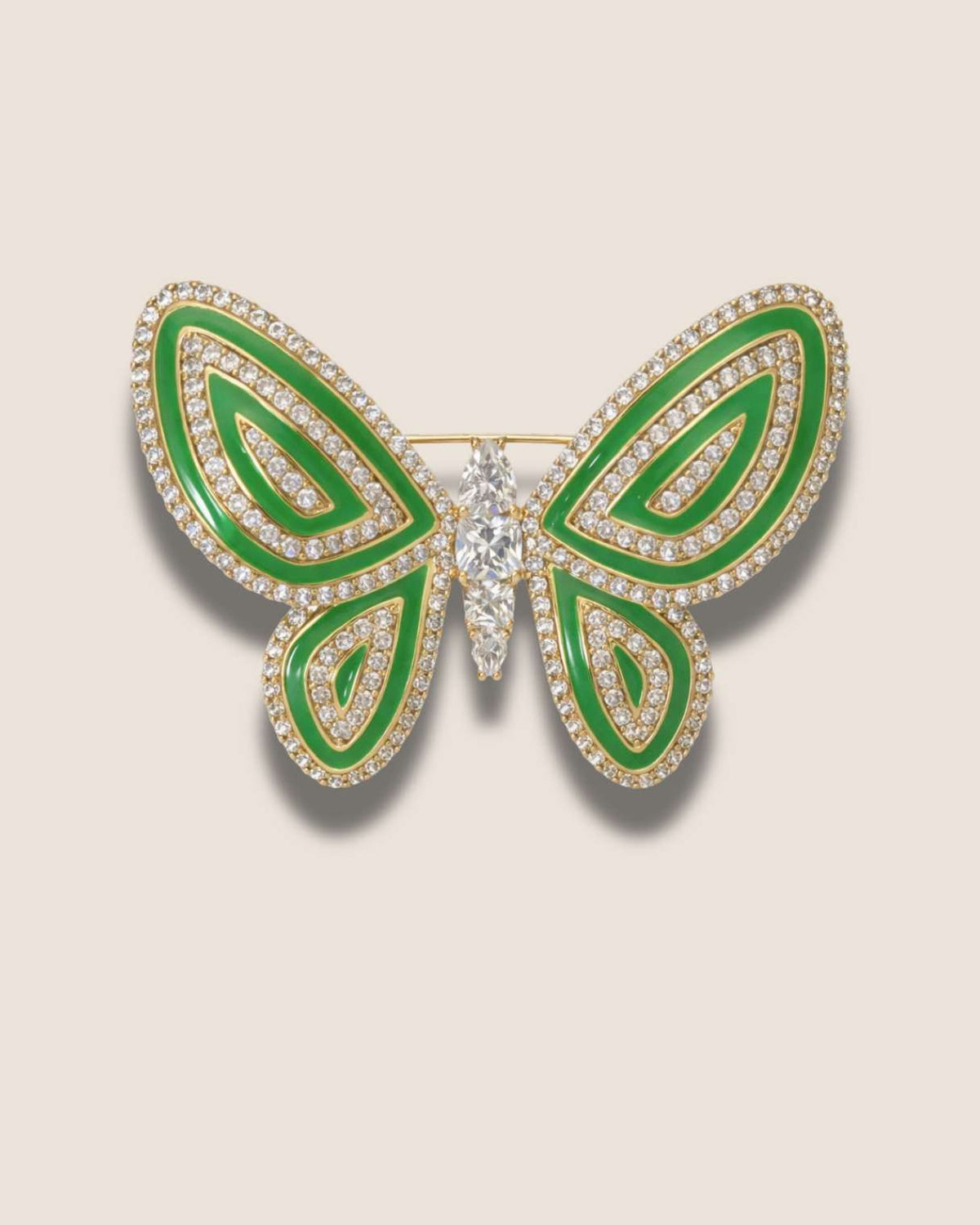 Butterfly-shaped brooch with green enamel and clear gemstones on a beige background