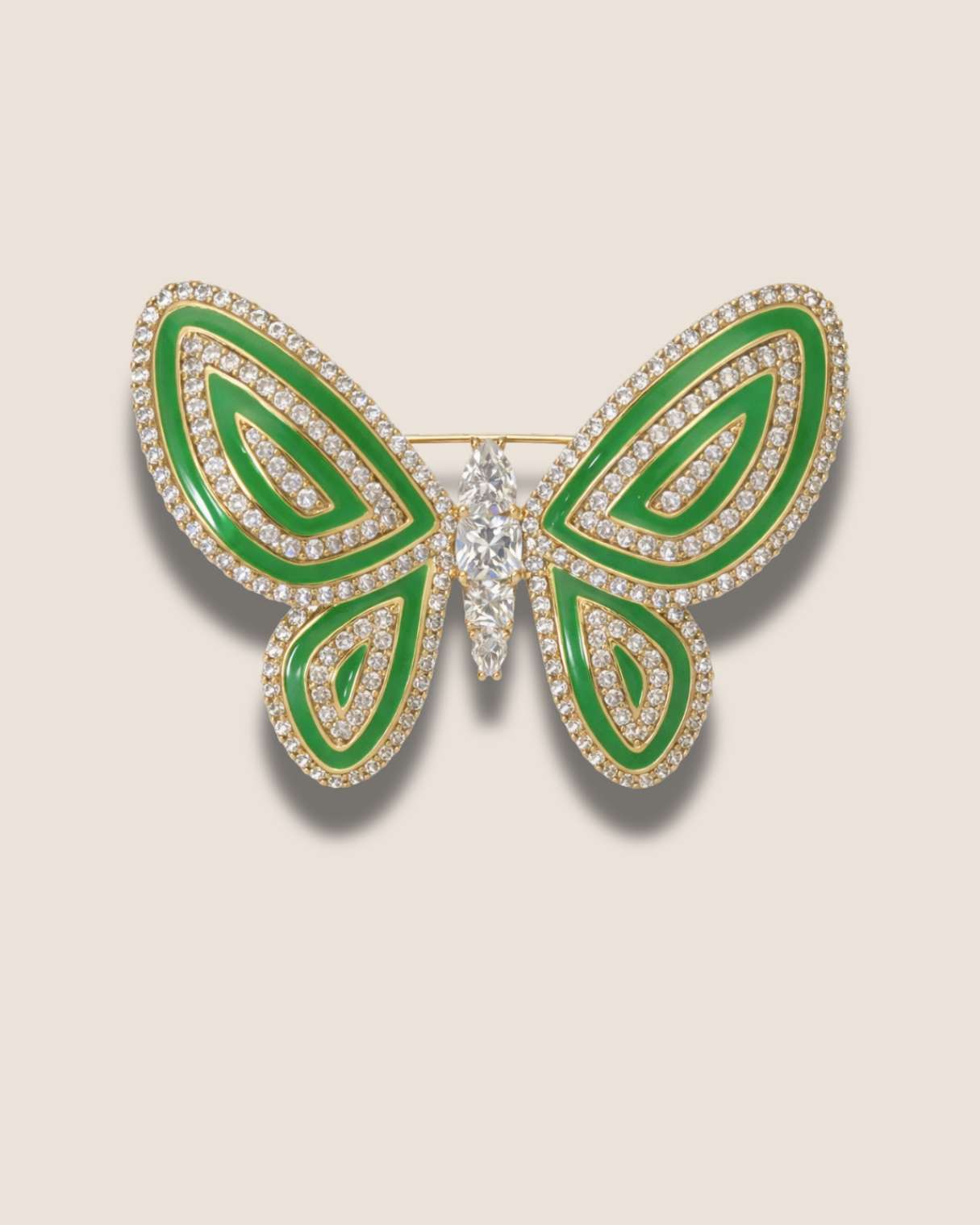 Butterfly-shaped brooch with green enamel and clear gemstones on a beige background