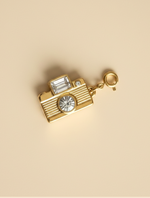 Gold camera-shaped charm with crystals on a beige background